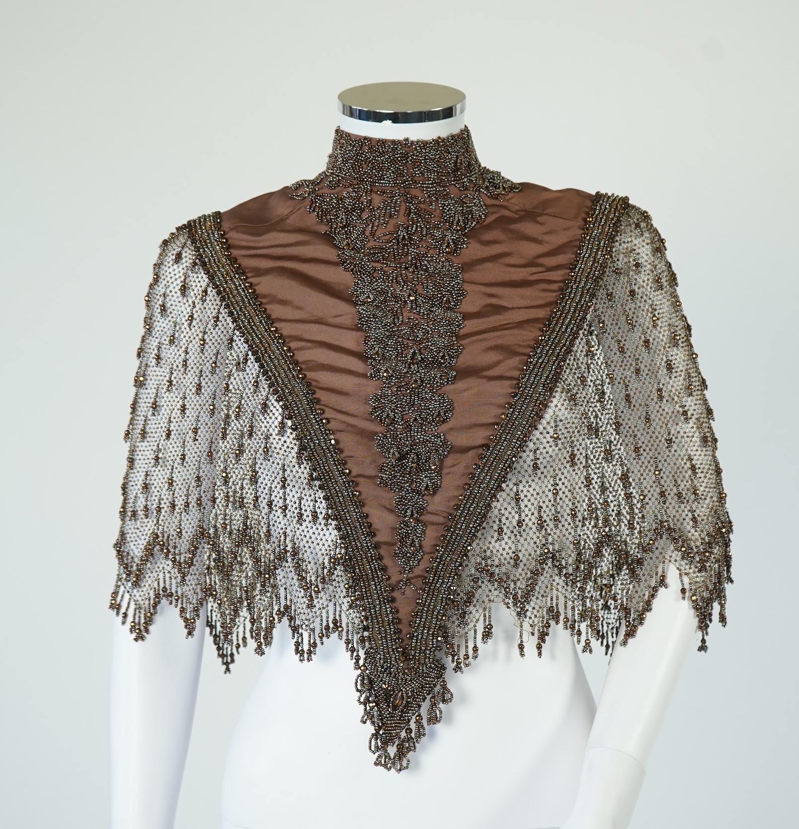 A late 19th century ladies ornate steel and brown beaded and fringed shoulder cape. Made as three ribbed silk panels with ornate beaded appliqués with a beaded and fringed net sleeved cape. Top of neck to bottom of beadi
